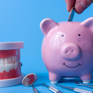 A piggy bank on a blue background next to several dental instruments