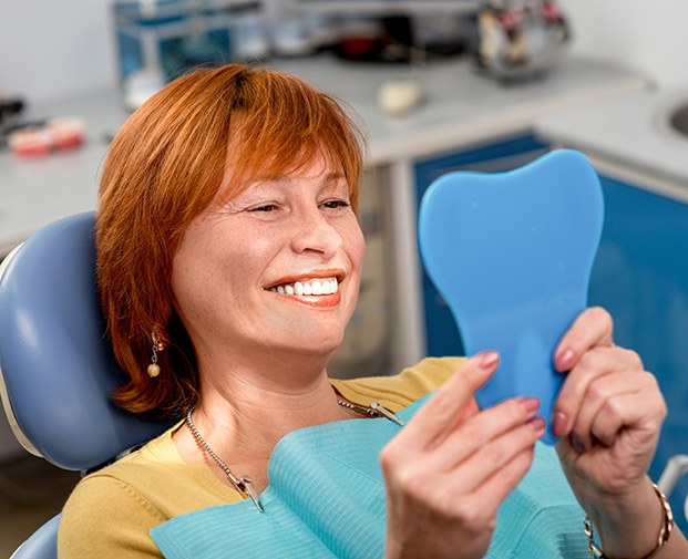 An older woman admiring her smile with a hand mirror