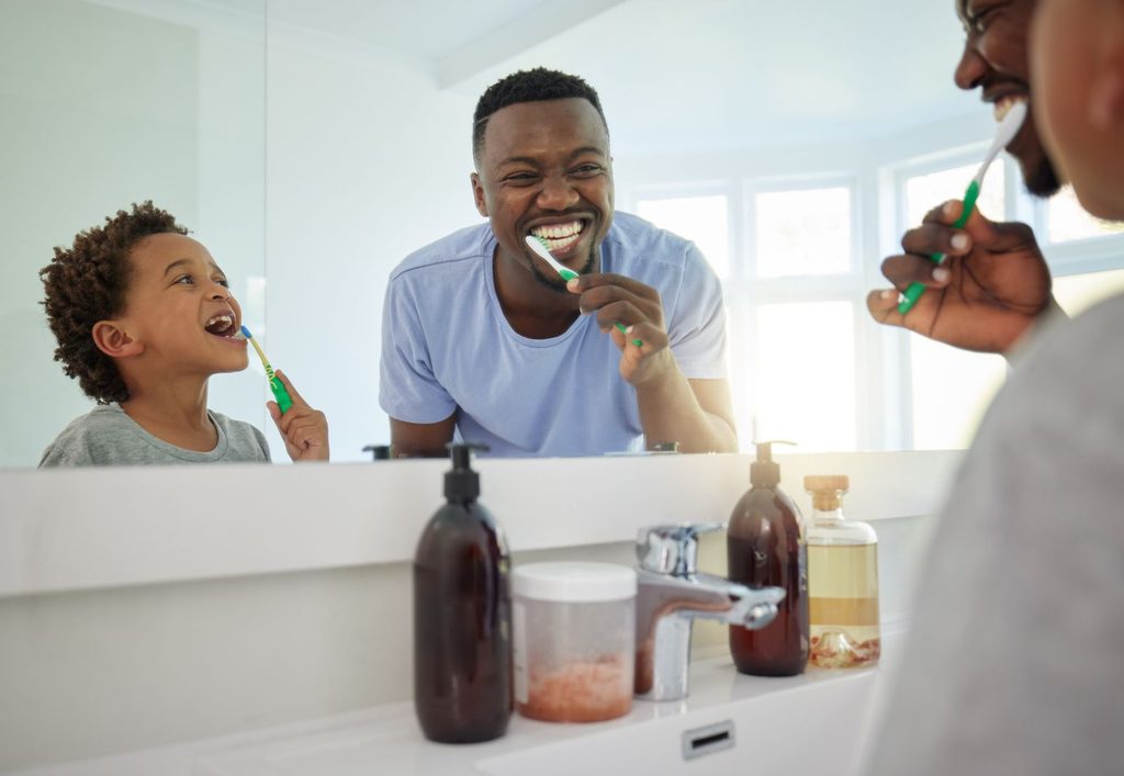 A man and his son brushing their teeth together.